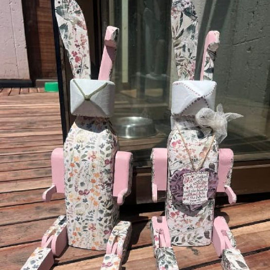 Two floral-patterned rabbit figurines with pink accents on a wooden surface.